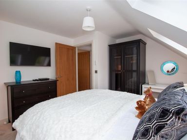 A bedroom with a bed white bedding black dresser blue vase wall mounted television black wardrobe small desk and round mirror at The Arthouse in Ambleside