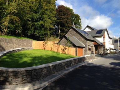 A stone house with a wooden fence and a curved stone wall around a grass lawn at The Arthouse in Ambleside