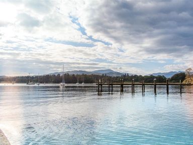 A lake with boats near a wooden pier and hills in the background at The Arthouse in Ambleside