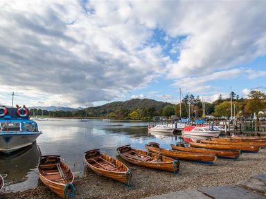 Wooden boats lined up on a shore with a lake and sailboats in the background at The Arthouse in Ambleside