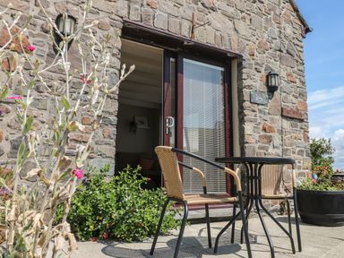 A stone patio with two wicker chairs and a round table outside a building with glass double doors at Carreg Ddu in Solva