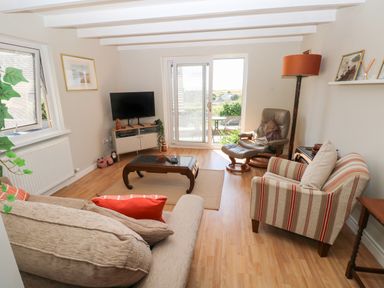 A living room with a sofa, armchair, coffee table, TV, floor lamp, and sliding glass door at Carreg Ddu in Solva