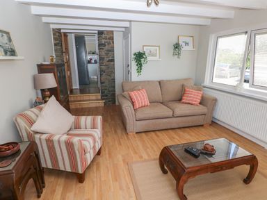 A living room with a striped armchair a beige sofa two shelves with plants and pictures and a wooden coffee table at Carreg Ddu in Solva