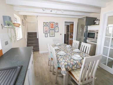 A kitchen dining area with a table set for six and a staircase in the background at Carreg Ddu in Solva