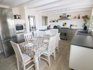 A kitchen with a dining table set with plates and glasses fridge oven and sink at Carreg Ddu in Solva