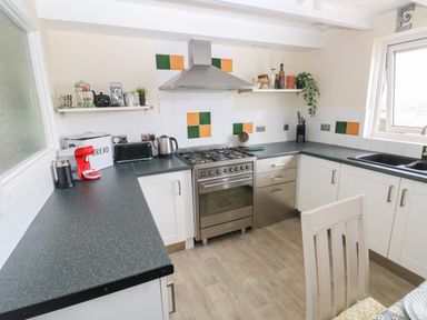 A kitchen with white cabinets a stainless steel stove and a black sink at Carreg Ddu in Solva