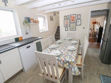 A kitchen with a dining table set for six chairs next to a dishwasher and refrigerator at Carreg Ddu in Solva