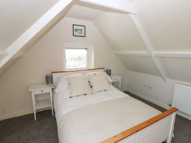A bedroom with a double bed white bedside tables and lamps under a sloped ceiling at Carreg Ddu in Solva