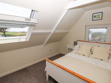A bedroom with a bed table lamp and windows showing an outside view at Carreg Ddu in Solva