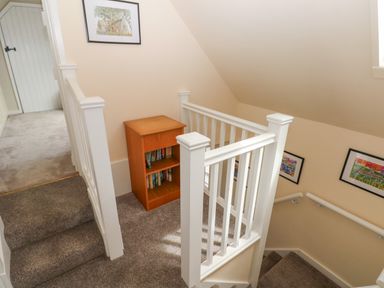 A stairwell with white railing carpeted stairs and a wooden bookshelf with books at Carreg Ddu in Solva