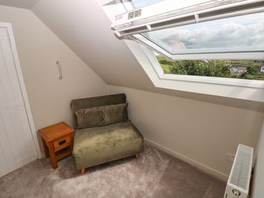 A small room with a green chair and wooden side table under a skylight window at Carreg Ddu in Solva