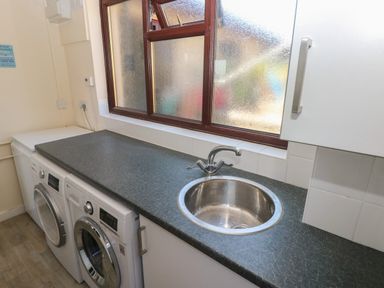 A utility room with washing machine dryer and sink under frosted windows at Carreg Ddu in Solva