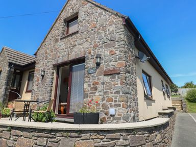 A stone and plaster exterior of a house with a small patio table and chairs at Carreg Ddu in Solva