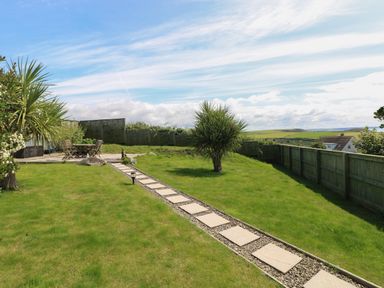 A garden with a stone pathway leading to outdoor seating and fenced surroundings at Carreg Ddu in Solva