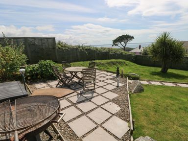 An outdoor patio with a round table and chairs a barbecue grill a grassy yard with trees and a fence at Carreg Ddu in Solva