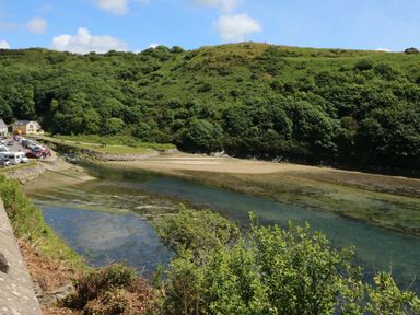 A river with sandy banks surrounded by green hills and trees with cars parked near a house at Carreg Ddu in Solva