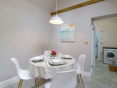 A dining area with a round table covered with a polka dot tablecloth and set for four with white chairs at West View in Feltwell