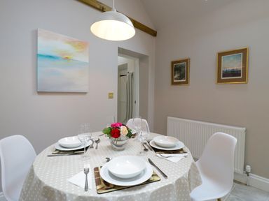 A dining room with a round table set for four people with plates glasses and cutlery and three framed pictures on the wall at West View in Feltwell