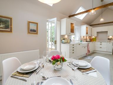 A kitchen and dining area with a round table set with plates glasses and cutlery and white cabinets under skylights at West View in Feltwell