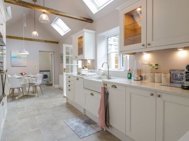 A kitchen with white cabinets a double sink and countertop appliances next to a dining table with chairs at West View in Feltwell