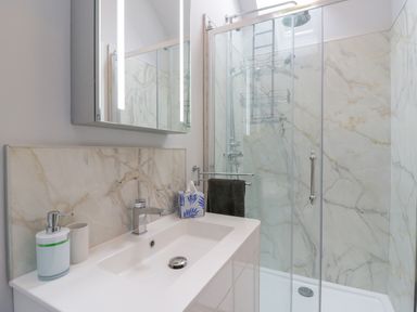 A bathroom with a white sink cabinet a soap dispenser a tissue box a glass shower with marble walls and a mirror cabinet at West View in Feltwell