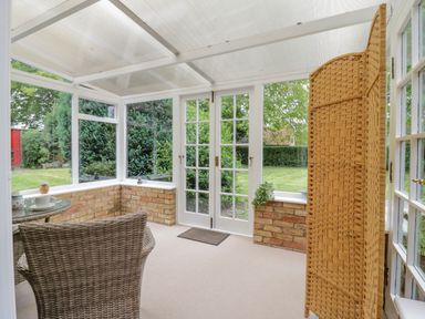A conservatory with wicker chairs a folding screen and glass doors opening to a garden at West View in Feltwell
