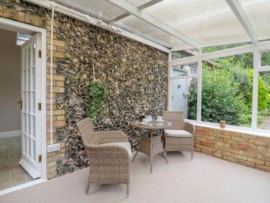 A conservatory with two wicker chairs and a small glass table against a stone wall at West View in Feltwell