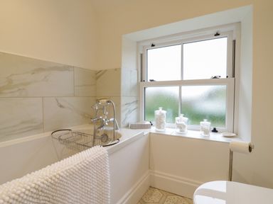 A bathroom with a bathtub a towel hanging on the tub and jars on the window sill at West View in Feltwell
