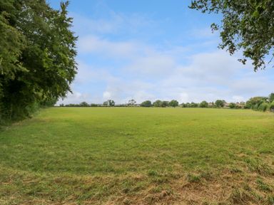 A large grassy field bordered by trees and houses in the distance at West View in Feltwell