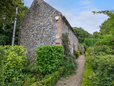 A stone cottage with a gravel pathway and green bushes at West View in Feltwell