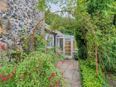 A garden path with a red metal arch and flowering plants leading to a conservatory at West View in Feltwell
