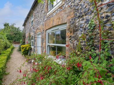 A stone and brick house exterior with flowers and bushes along a gravel path at West View in Feltwell