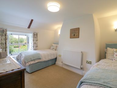 A bedroom with two single beds a window with floral curtains and a wooden chest of drawers at West View in Feltwell