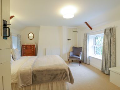 A bedroom with a bed a wooden chest of drawers a grey armchair and a window with curtains at West View in Feltwell
