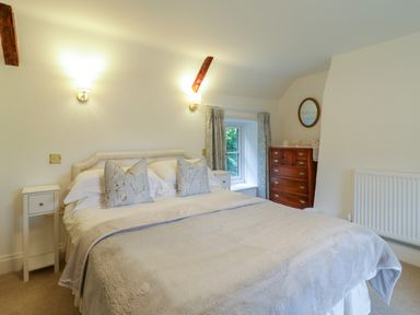 A bedroom with a double bed two nightstands window with curtains and a wooden dresser with a round mirror at West View in Feltwell