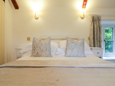 A bedroom with a made bed two floral pillows two bedside tables two wall lamps and a window with floral curtains at West View in Feltwell