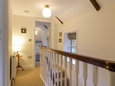A hallway with a wooden handrail and white balusters a small table with a lamp and a view into a bedroom at West View in Feltwell