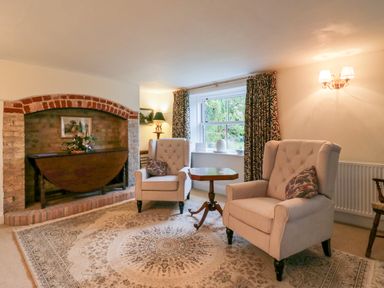 A sitting room with two upholstered armchairs a wooden side table an arched brick fireplace and a window with curtains at West View in Feltwell