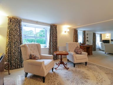 A sitting area with two armchairs and a small table in front of windows with patterned curtains at West View in Feltwell