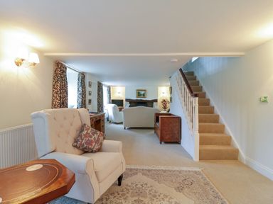 A sitting room with armchairs a wooden side table carpet and stairs at West View in Feltwell