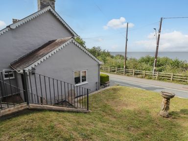A grassy yard with a birdbath and a white house near a road with a view of the sea