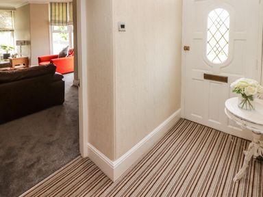 A hallway with striped carpet a white door and a small round table with flowers and a view into a living room with a brown sofa and an orange sofa at Morva in New Quay