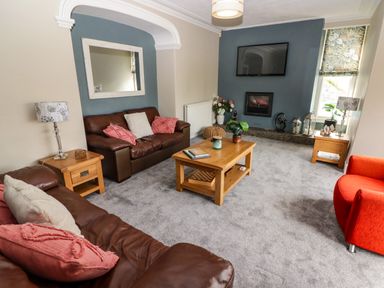 A living room with brown leather sofas a wooden coffee table a wall-mounted television and a fireplace at Morva in New Quay