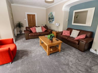 A living room with two brown leather sofas a red armchair a wooden coffee table and a plant at Morva in New Quay