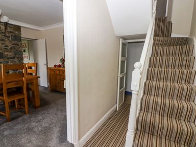 A hallway with striped carpeted stairs next to a dining area with wooden chairs and a sideboard at Morva in New Quay