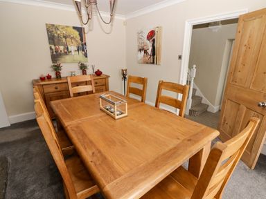 A dining room with a wooden table and chairs paintings on the wall and a sideboard at Morva in New Quay
