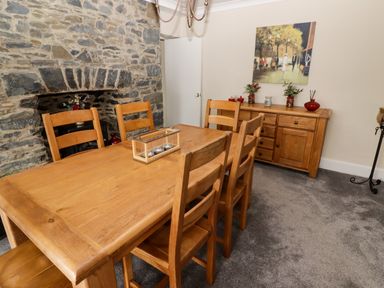 A dining room with a wooden table and chairs a stone wall with fireplace and a wooden sideboard with decorations at Morva in New Quay