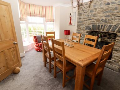 A dining room with a wooden table and six chairs next to a stone fireplace and a window with striped blinds at Morva in New Quay