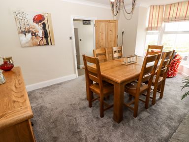 A dining room with a wooden table and six chairs next to a window with striped blinds at Morva in New Quay