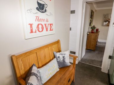 A wooden bench with three decorative cushions under a wall art with a cup and text there is love at Morva in New Quay